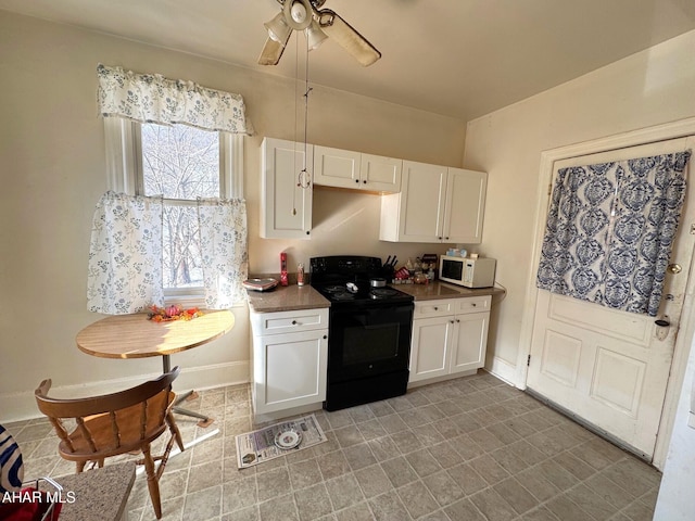 kitchen with white microwave, black range with electric cooktop, baseboards, white cabinets, and dark countertops