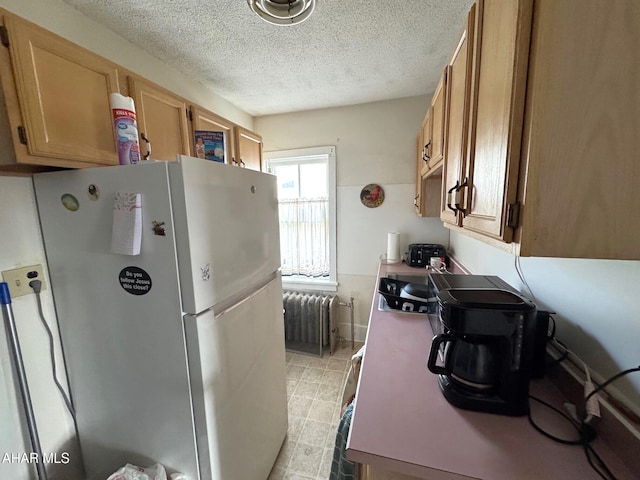 kitchen with radiator, a textured ceiling, and freestanding refrigerator