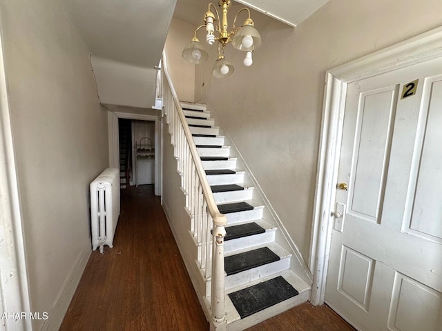 staircase featuring baseboards, a notable chandelier, wood finished floors, and radiator