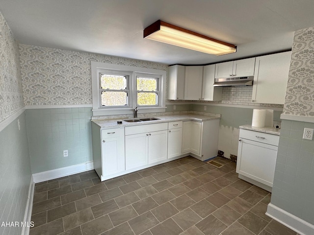 kitchen featuring white cabinets, a sink, under cabinet range hood, and wallpapered walls