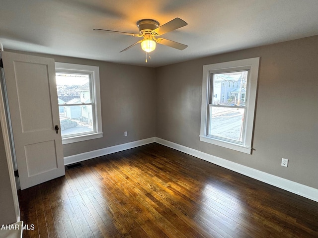 spare room with dark wood-style flooring, a healthy amount of sunlight, visible vents, and baseboards