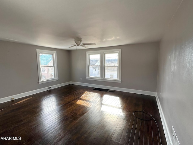 spare room with a ceiling fan, dark wood-style flooring, visible vents, and baseboards