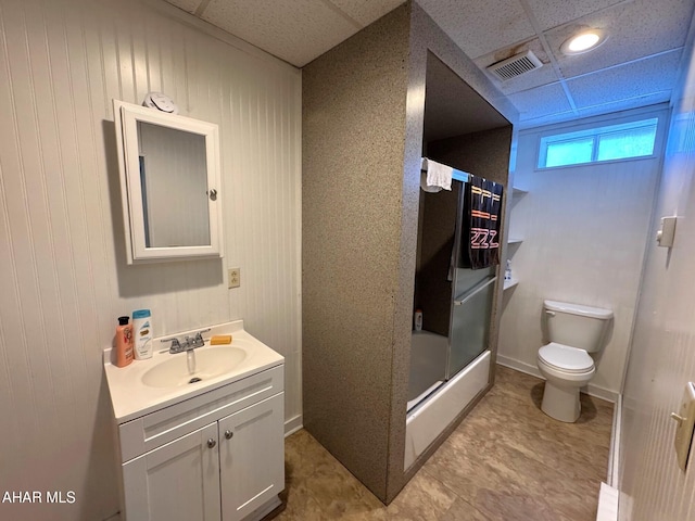 bathroom featuring bath / shower combo with glass door, a paneled ceiling, visible vents, toilet, and vanity