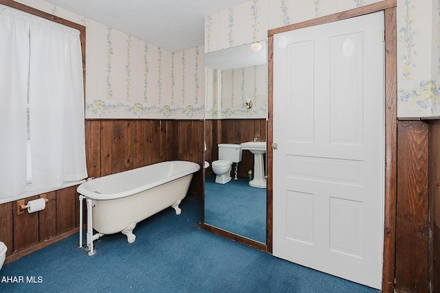 bathroom featuring a tub to relax in, wood walls, a textured ceiling, and toilet