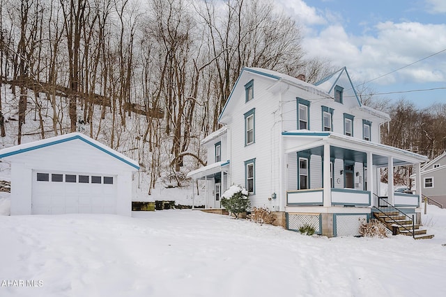 snow covered property featuring a garage, an outdoor structure, and covered porch