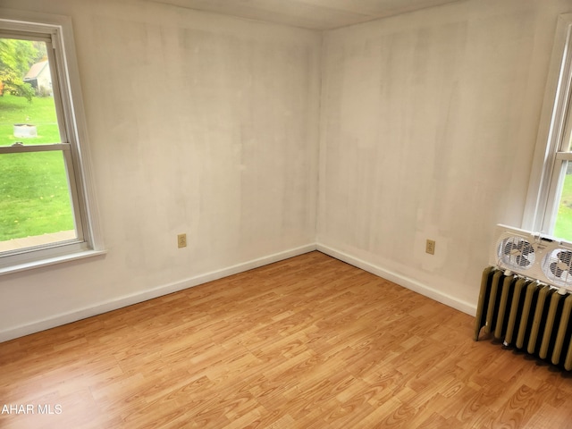 unfurnished room featuring radiator heating unit, a healthy amount of sunlight, and light hardwood / wood-style floors