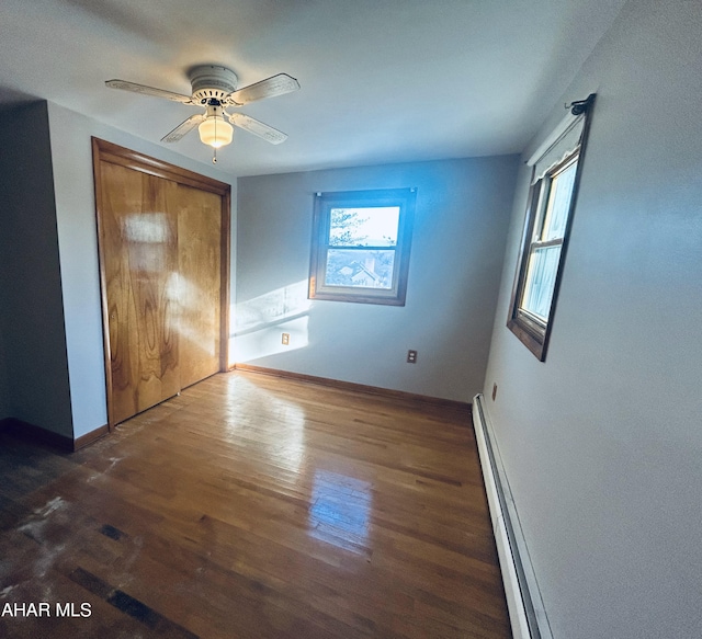 unfurnished bedroom with ceiling fan, a closet, dark hardwood / wood-style floors, and a baseboard heating unit