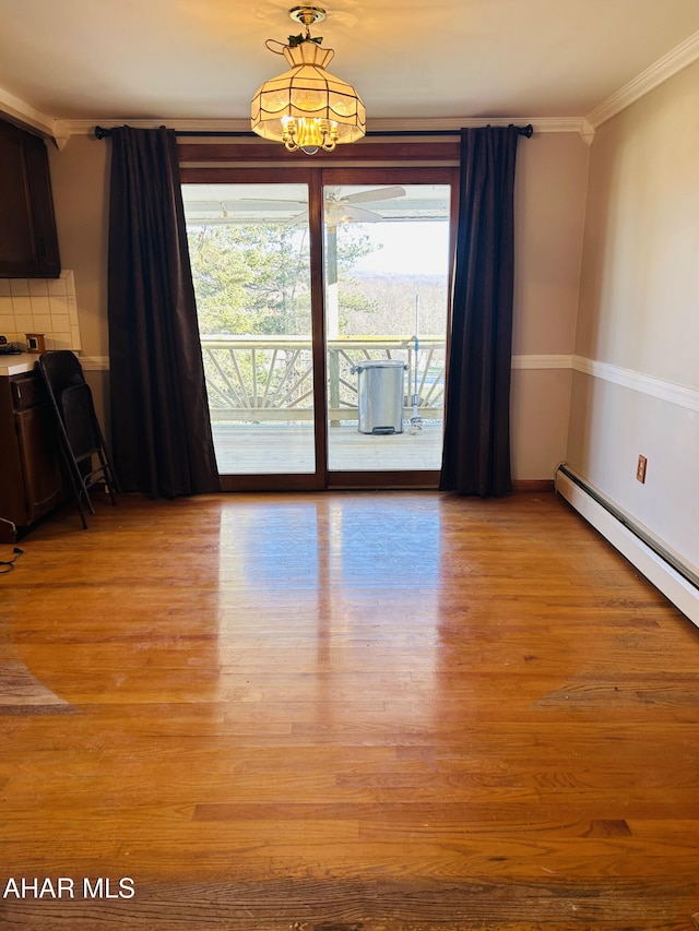 unfurnished dining area featuring a chandelier, light wood-type flooring, a baseboard radiator, and crown molding