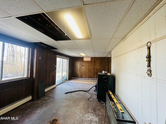 basement featuring a wealth of natural light, a drop ceiling, and wood walls