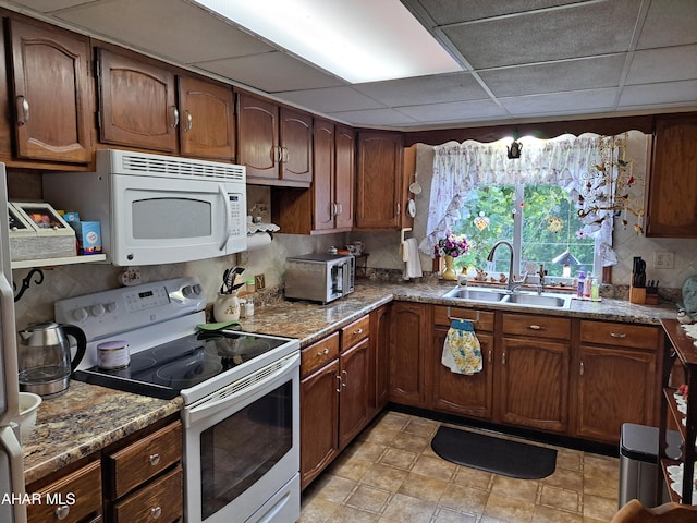 kitchen with backsplash, a paneled ceiling, dark stone counters, white appliances, and sink