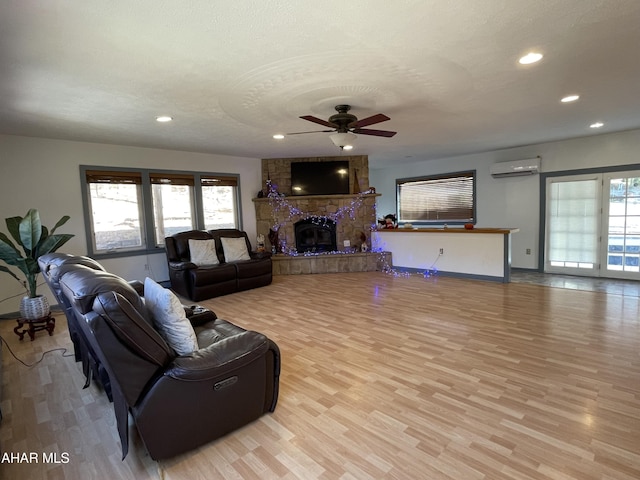 living room with a wall mounted AC, ceiling fan, light hardwood / wood-style flooring, and plenty of natural light