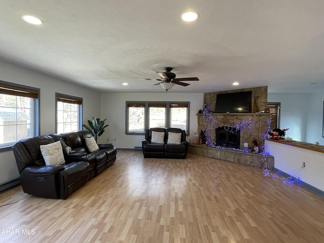 living room featuring a fireplace, ceiling fan, a textured ceiling, and light hardwood / wood-style flooring