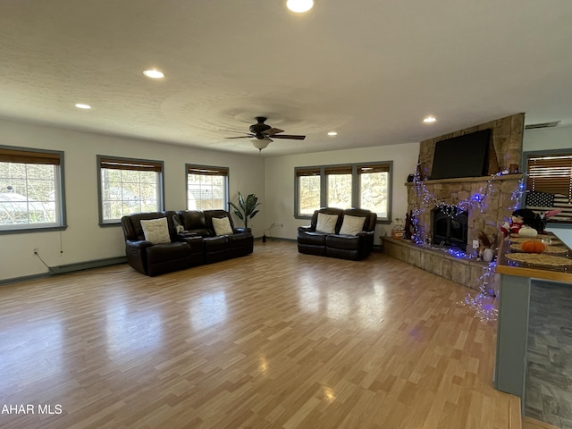 living room with a stone fireplace, ceiling fan, light hardwood / wood-style flooring, and a textured ceiling