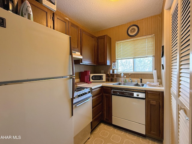 kitchen featuring sink, white appliances, a textured ceiling, and wood walls