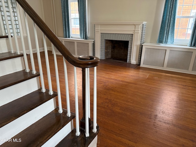 stairway featuring radiator heating unit, a fireplace, and wood finished floors