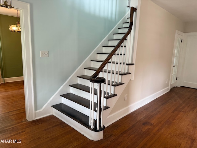 stairway with baseboards, a notable chandelier, and wood finished floors