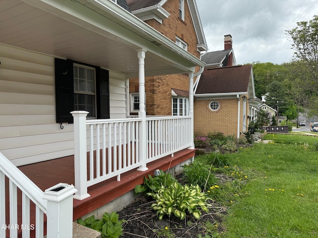 view of side of home featuring covered porch, brick siding, and a lawn
