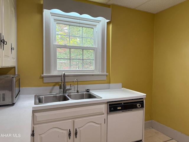 kitchen with light countertops, stainless steel microwave, a sink, and white dishwasher