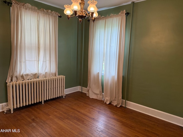 empty room featuring a chandelier, radiator, baseboards, and dark wood-style flooring