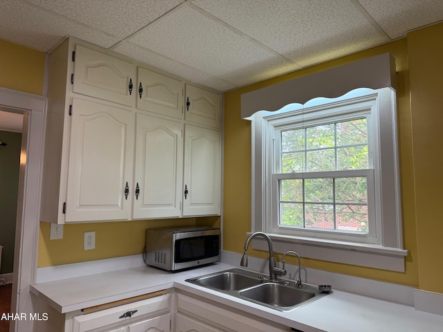 kitchen with a paneled ceiling, light countertops, a sink, and stainless steel microwave