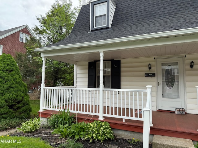 doorway to property with a porch and a shingled roof