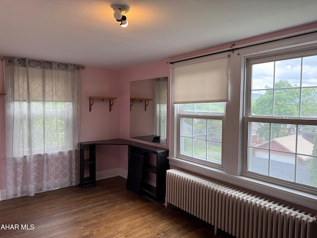 unfurnished office featuring baseboards, radiator, and wood finished floors