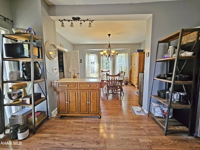 kitchen featuring wood finished floors, light countertops, a chandelier, brown cabinets, and decorative light fixtures