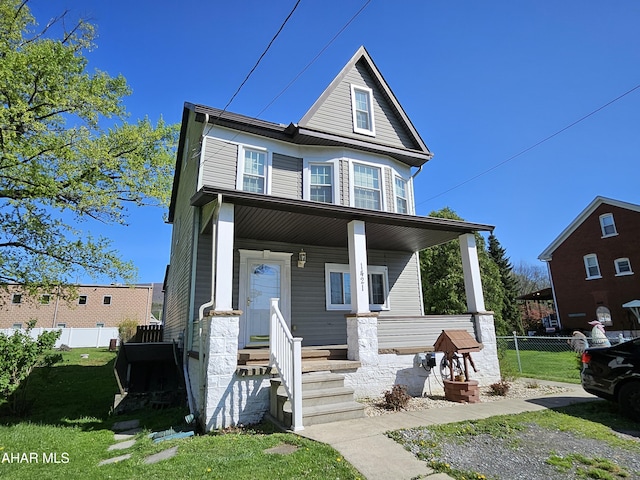 traditional home featuring a porch, fence, and a front lawn