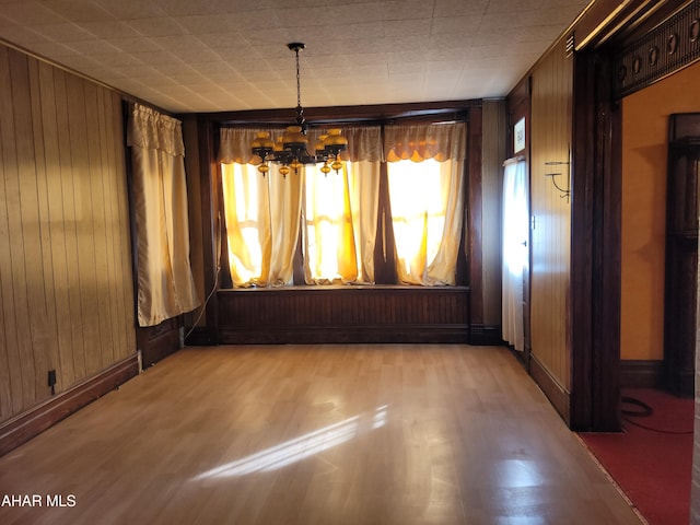 unfurnished dining area featuring a chandelier, hardwood / wood-style flooring, and wood walls