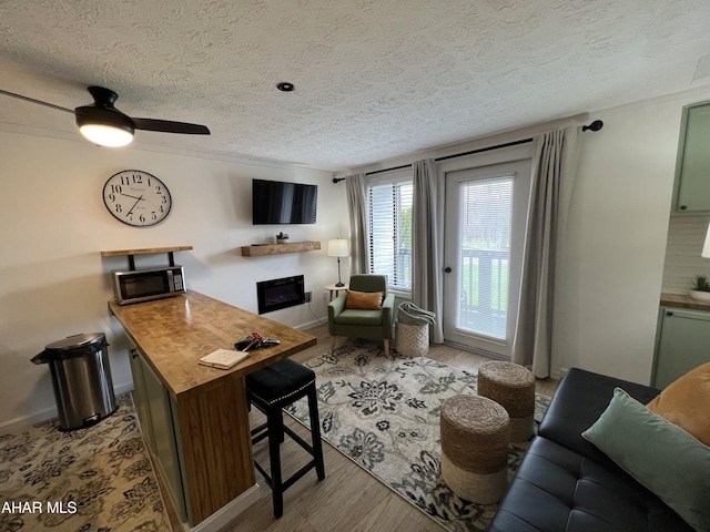 living room with ceiling fan, a textured ceiling, and light wood-type flooring