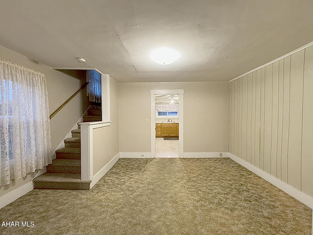 carpeted spare room with wood walls, stairs, and baseboards