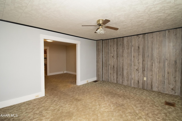 carpeted empty room featuring crown molding, wooden walls, and ceiling fan