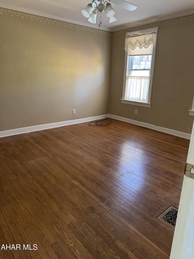 empty room featuring dark wood-style floors, crown molding, visible vents, a ceiling fan, and baseboards