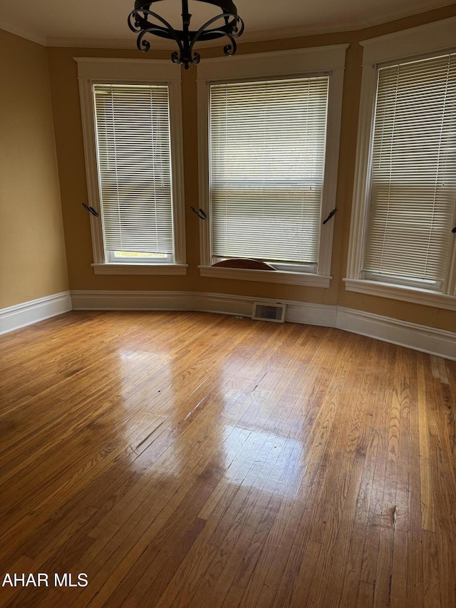 empty room featuring baseboards, visible vents, hardwood / wood-style flooring, ornamental molding, and a chandelier