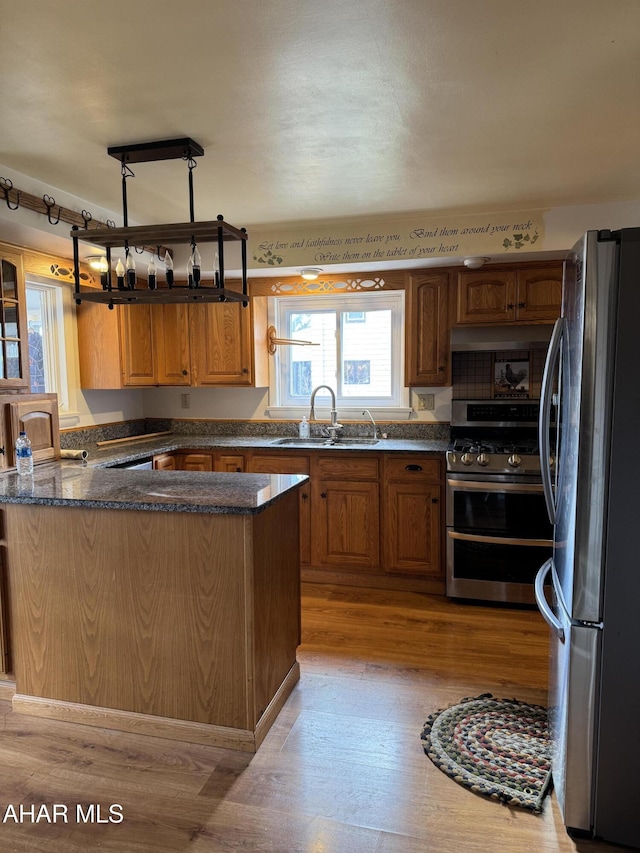 kitchen featuring stainless steel appliances, a sink, light wood-type flooring, brown cabinetry, and dark stone countertops