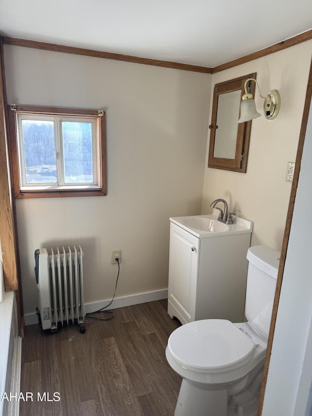 half bathroom with toilet, radiator heating unit, vanity, wood finished floors, and baseboards