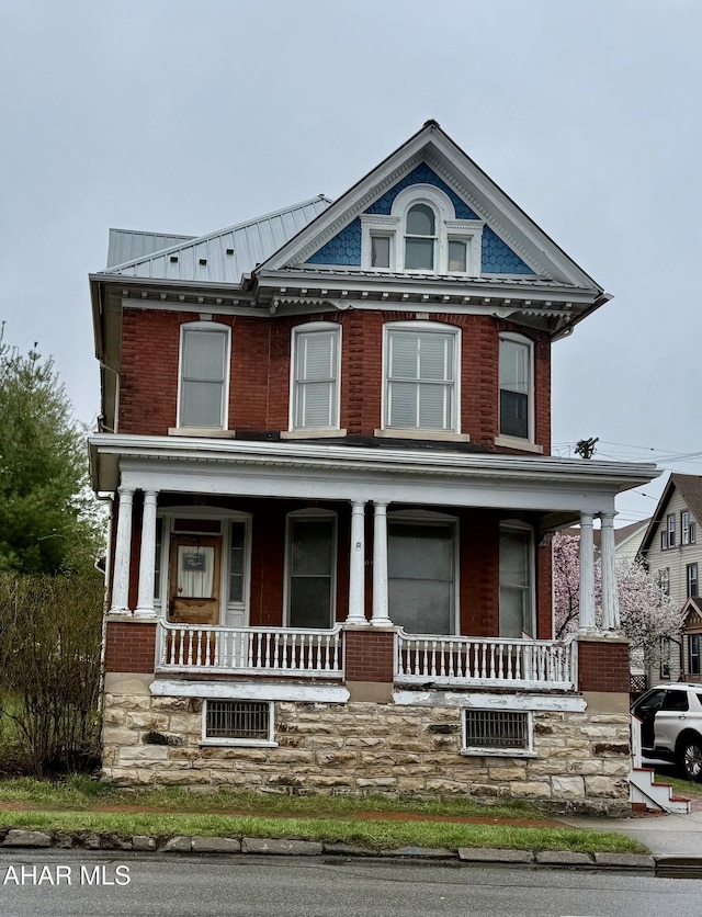 view of front of house featuring brick siding, a porch, and metal roof