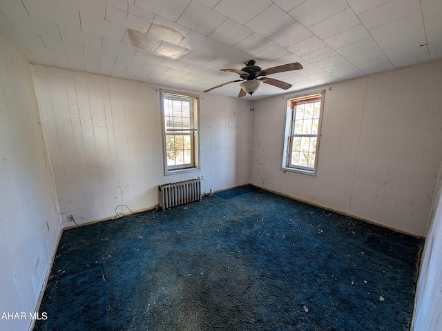 carpeted spare room featuring radiator heating unit, ceiling fan, and a healthy amount of sunlight