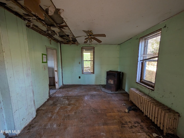 unfurnished living room with ceiling fan, radiator heating unit, dark wood-type flooring, and a wood stove