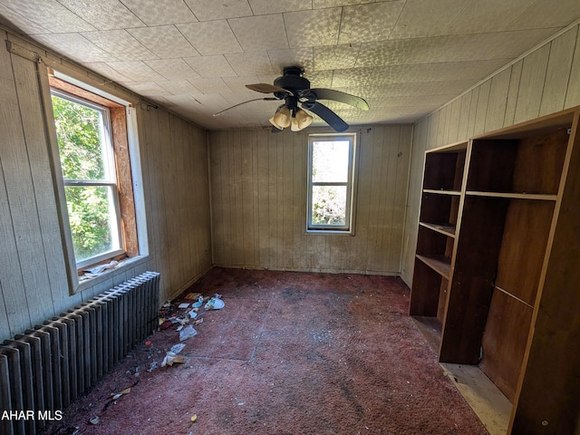 carpeted empty room with wood walls, radiator heating unit, and ceiling fan