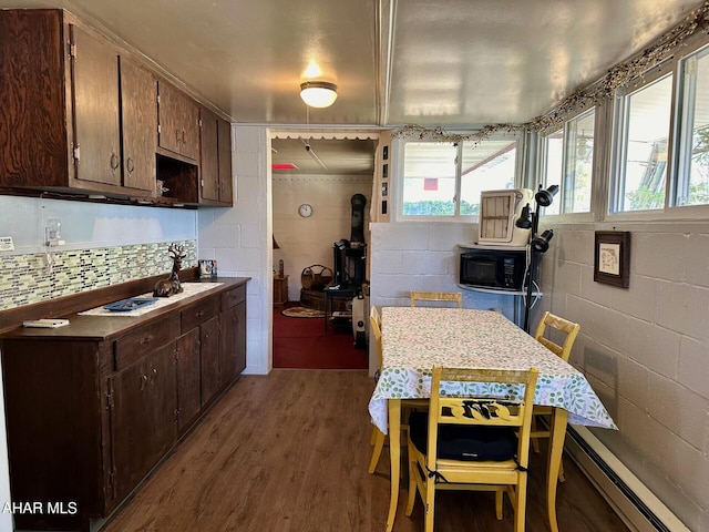 kitchen featuring dark brown cabinetry, wood-type flooring, baseboard heating, and a wood stove