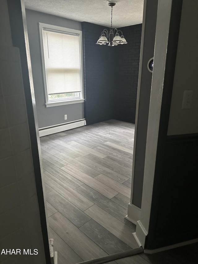 unfurnished room with baseboard heating, hardwood / wood-style floors, a chandelier, and a textured ceiling