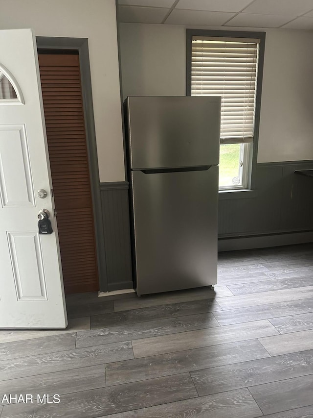 kitchen with baseboard heating, stainless steel refrigerator, a paneled ceiling, and hardwood / wood-style flooring