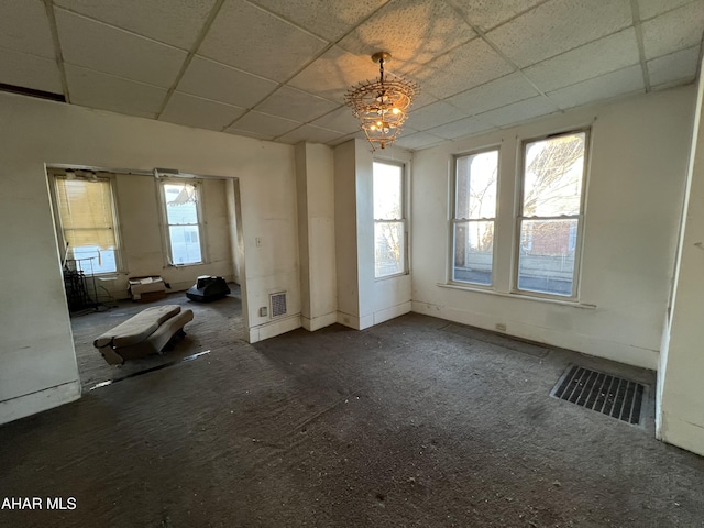 interior space with a paneled ceiling, dark carpet, and an inviting chandelier