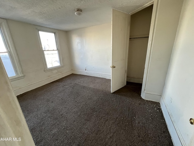 unfurnished bedroom featuring a textured ceiling, dark carpet, and a closet