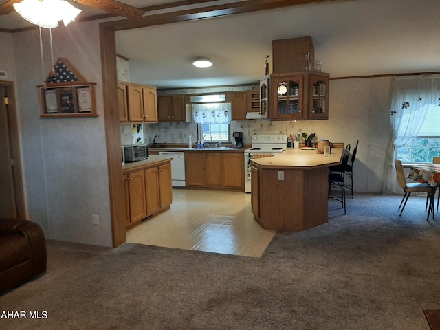 kitchen featuring a breakfast bar, white appliances, sink, a kitchen island, and light colored carpet