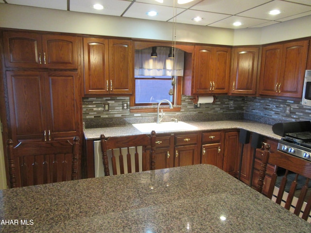 kitchen with pendant lighting, stone countertops, sink, and backsplash