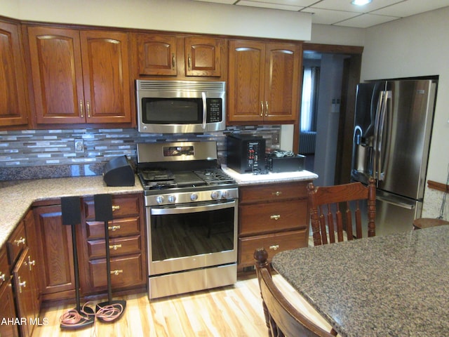 kitchen with decorative backsplash, appliances with stainless steel finishes, light wood-type flooring, and a drop ceiling