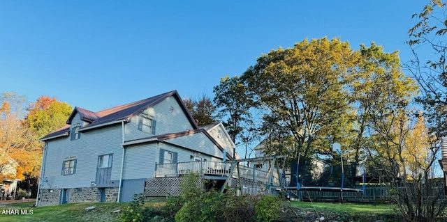 view of property exterior with a trampoline, a yard, and a wooden deck