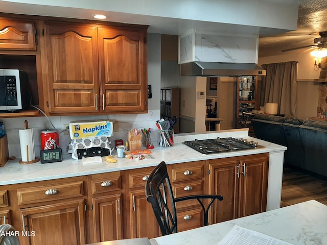 kitchen with hardwood / wood-style floors, stainless steel gas stovetop, ceiling fan, tasteful backsplash, and light stone counters